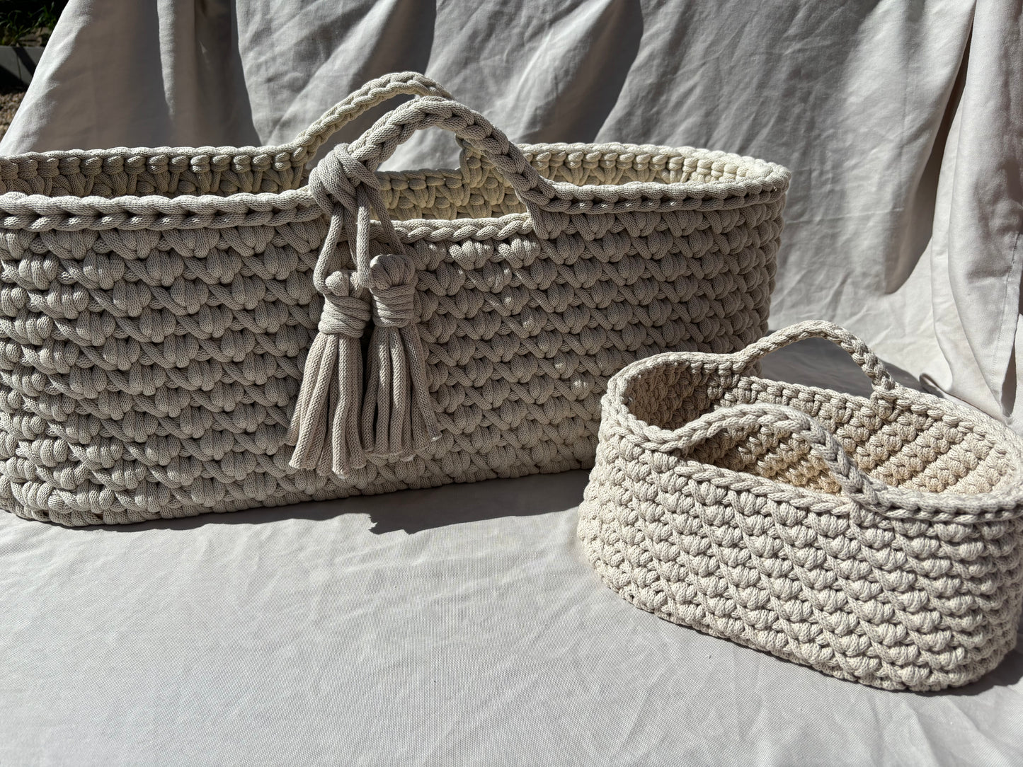 beige moses basket and nappy caddy side by side outside so you can see all the detail of the baskets and the crochet work