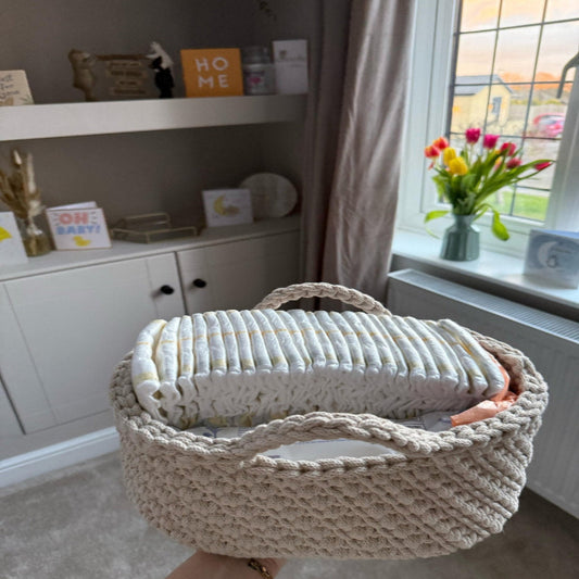 Person holding a crochet basket with nappies inside, in a room with a shelf and window.
