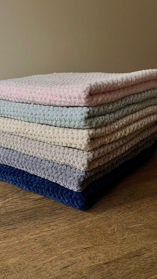 6 of the chunky blankets neatly sat on top of one another in the same way on a wooden table in a neutral space