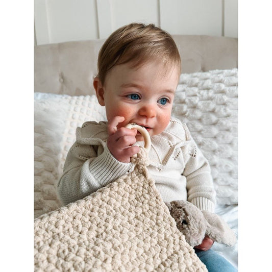 Baby holding a comforterand teething ring on a soft surface