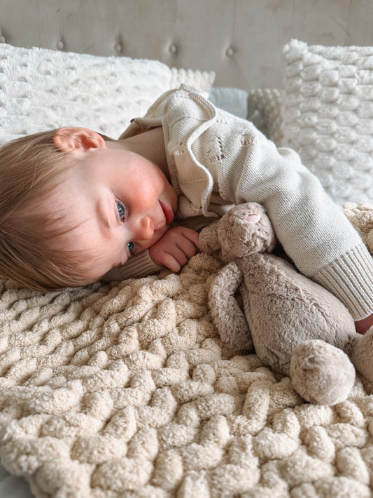 Toddler with the oatmeal super chunky blanket laid down with her teddy on the bed