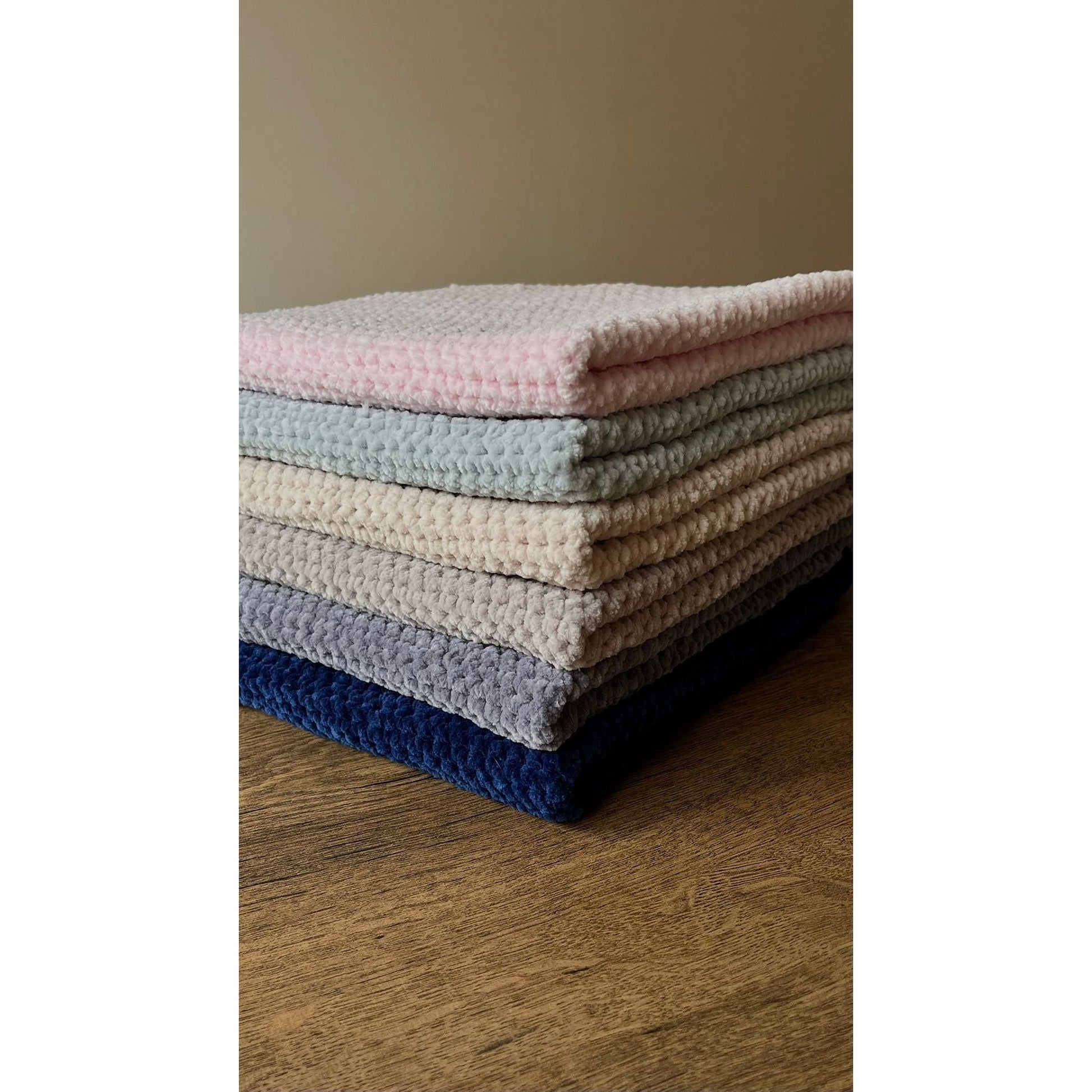 6 of the chunky blankets neatly sat on top of one another in the same way on a wooden table in a neutral space