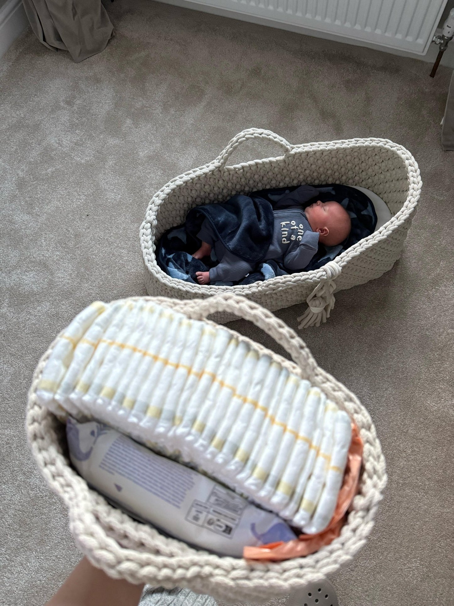 Two crochet baby items, nappy caddy and moses basket, with a baby inside on a carpeted floor