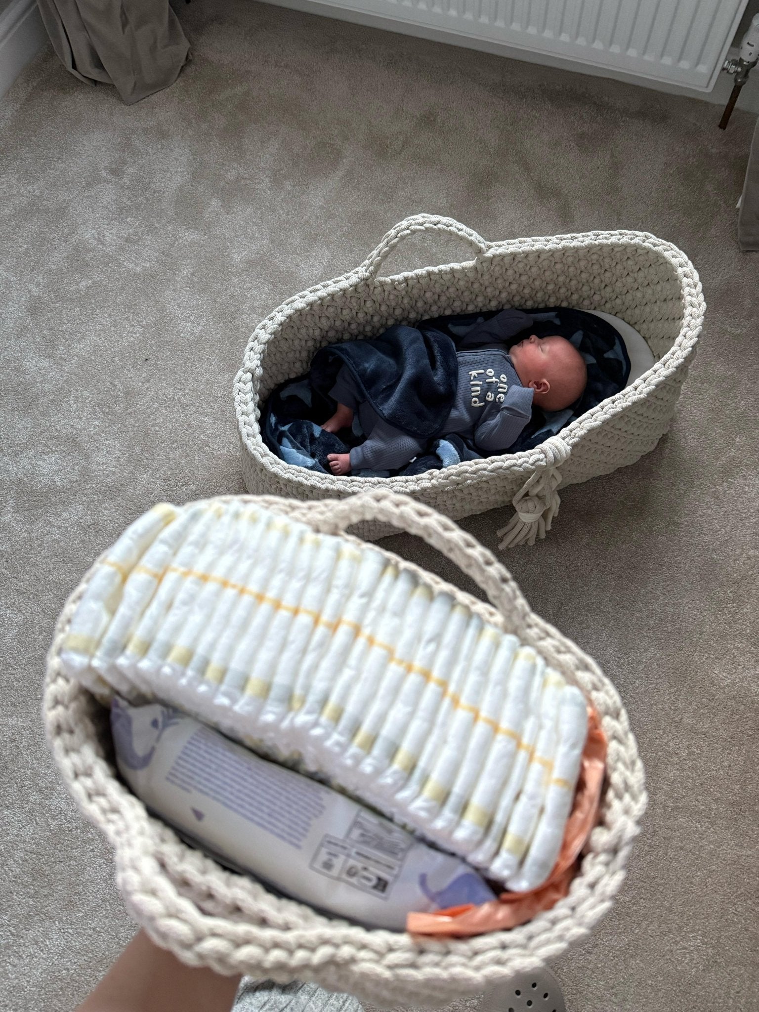 Two crochet baby items, nappy caddy and moses basket, with a baby inside on a carpeted floor