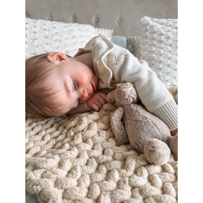 Toddler with the oatmeal super chunky blanket laid down with her teddy on the bed
